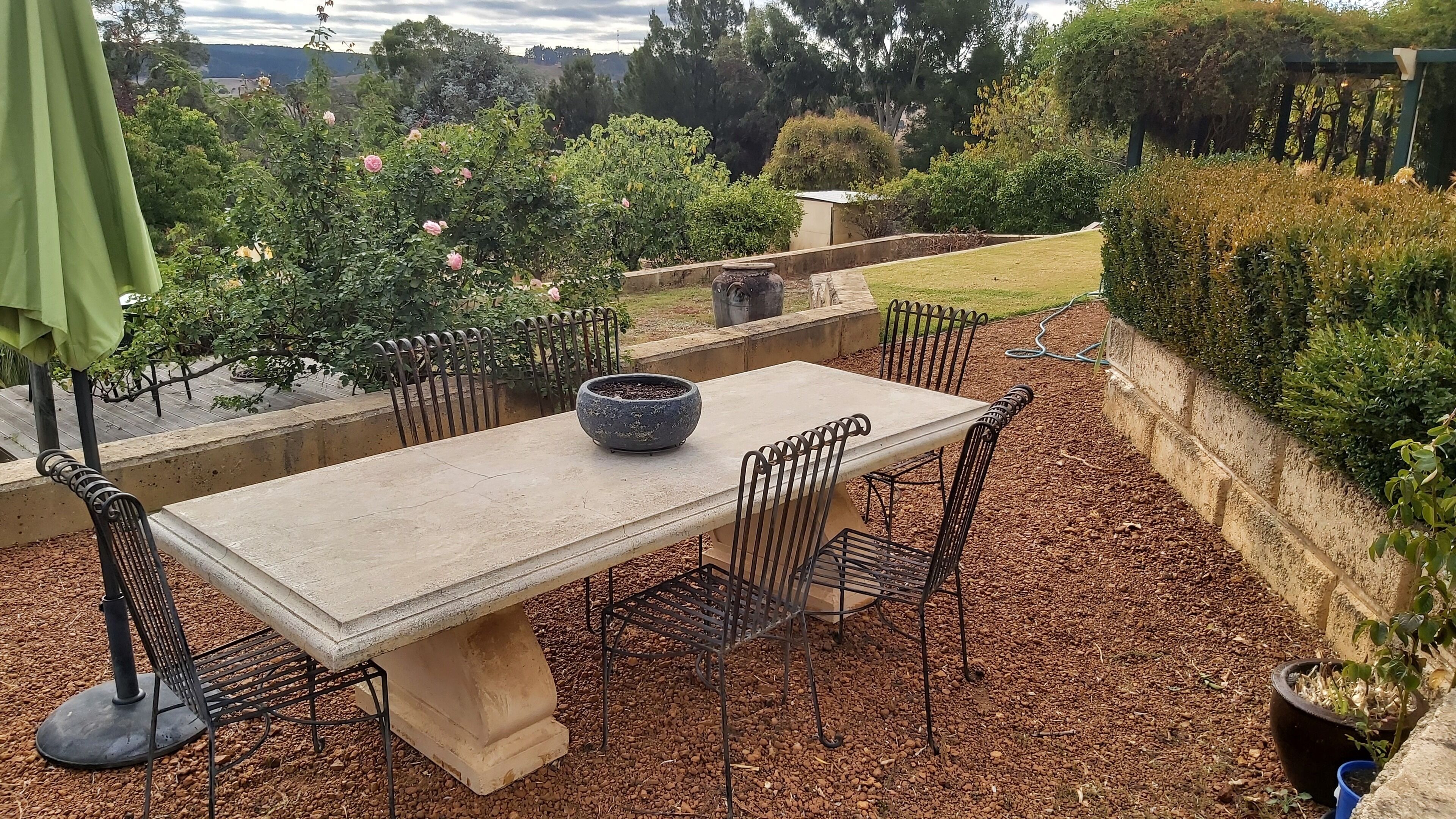 An outdoor patio with a table and chairs, surrounded by a garden with various plants and a view of the landscape.