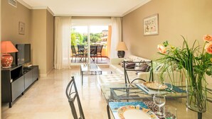 A modern living room with a TV, sofa, dining table, and a balcony with outdoor furniture.