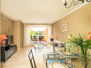 A modern living room with a TV, sofa, dining table, and a balcony with outdoor furniture.
