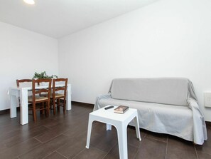 Uma sala de estar com um sofá, uma mesinha branca e duas cadeiras de madeira.