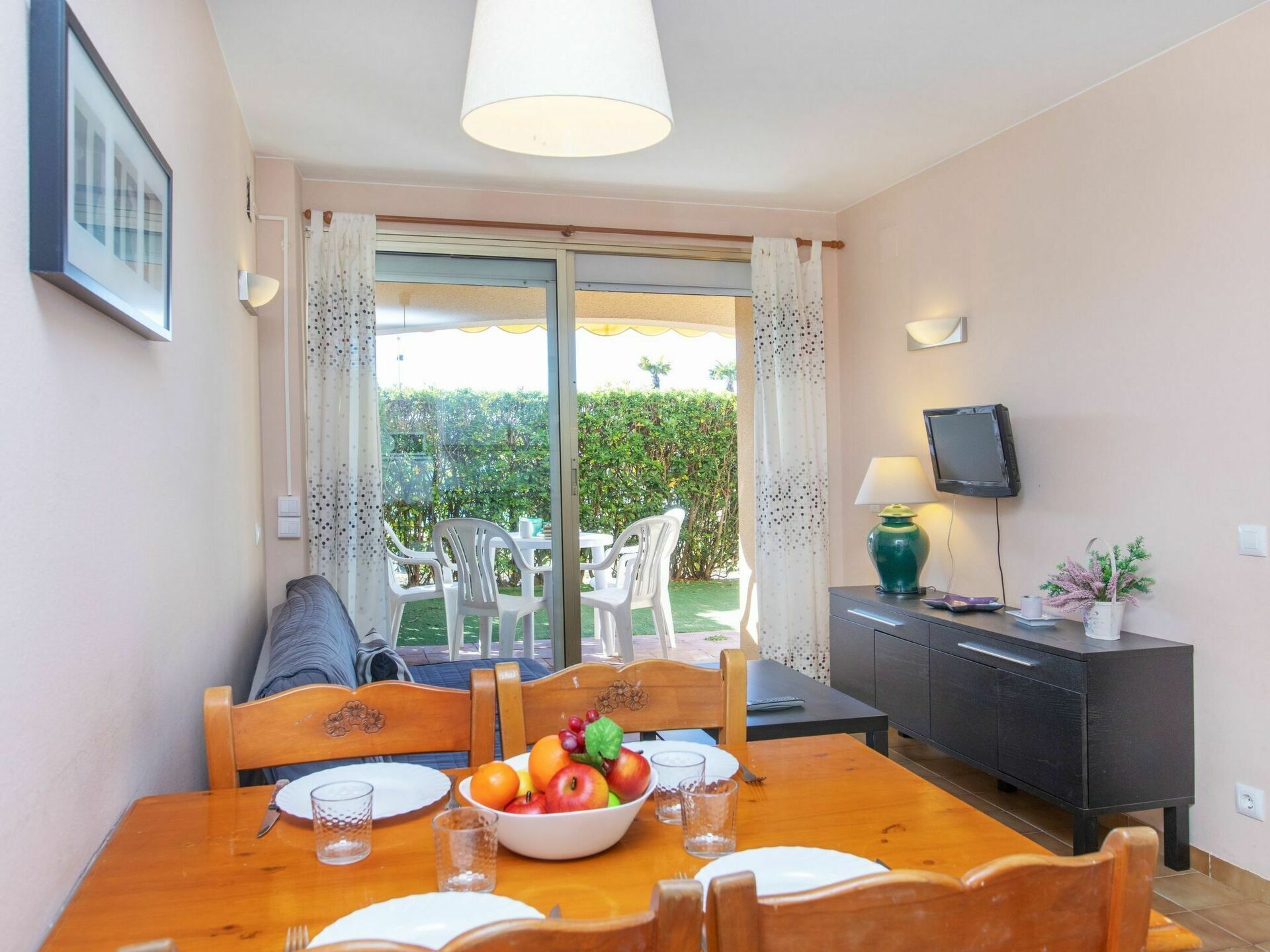 Un coin repas avec une table dressée pour quatre personnes, un saladier de fruits et un téléviseur posé sur un meuble.