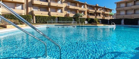 A clear swimming pool with metal ladders, surrounded by a multi-story building with balconies.