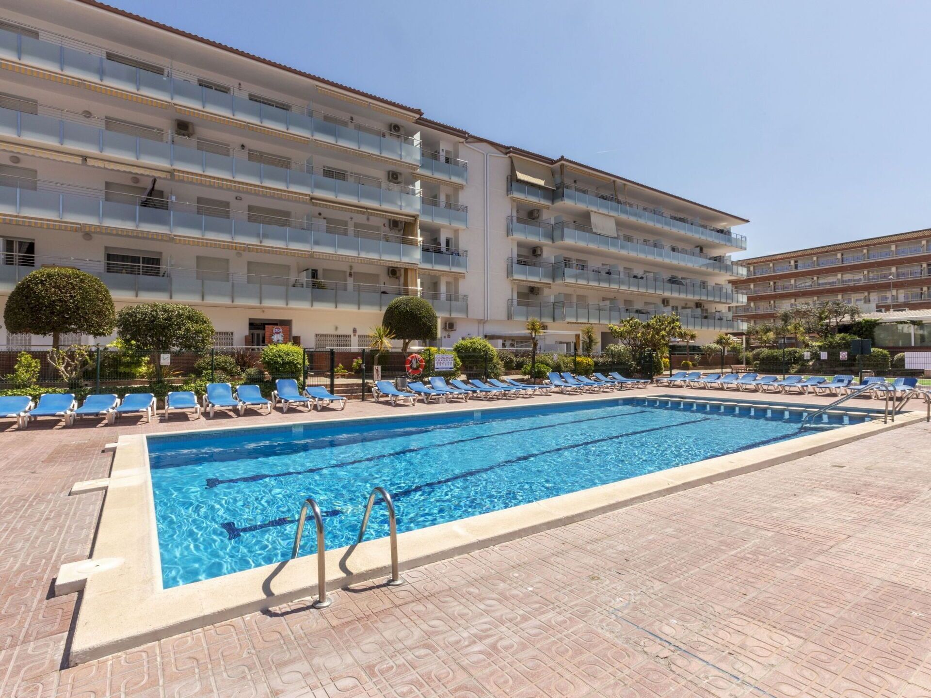 A hotel with a swimming pool, sun loungers, and a multi-story building with balconies.