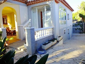 Una casa con facciata bianca, tetto in tegole e una scalinata in pietra che conduce a un portico con balaustra bianca.
