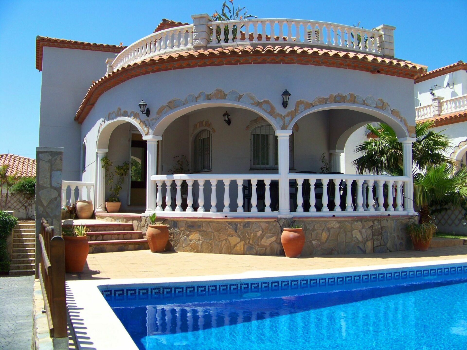 A two-story house with a swimming pool, stone steps, and a balcony with white balustrades.