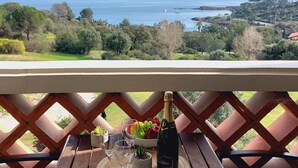Un balcon avec vue sur la mer, une bouteille de champagne et un panier de fruits.