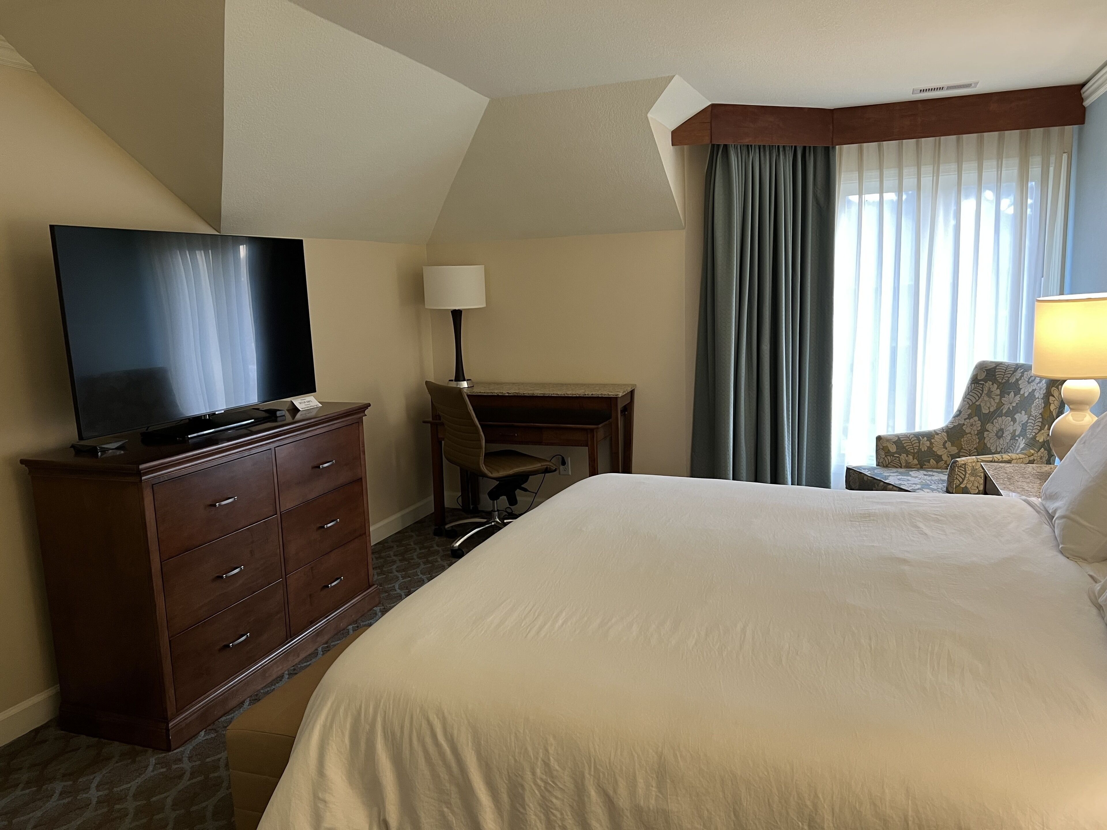 Quarto de hotel com uma cama grande, uma escrivaninha, uma televisão e uma cadeira.