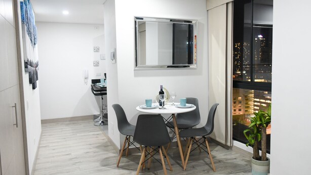 Un'area pranzo moderna con un tavolo rotondo, quattro sedie, uno specchio e vista sulla città attraverso una finestra.