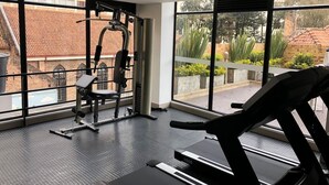 Una palestra con attrezzature per esercizi, ampie finestre e vista su edifici e vegetazione.