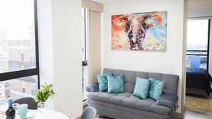 Un soggiorno moderno con un divano grigio, cuscini color acquamarina, un quadro astratto dai colori vivaci e un'area pranzo con un tavolo apparecchiato per due.