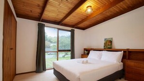 Ein Schlafzimmer mit Bett, Holz-Kopfteil, Nachttisch, einem Gemälde und Blick durch ein Fenster.