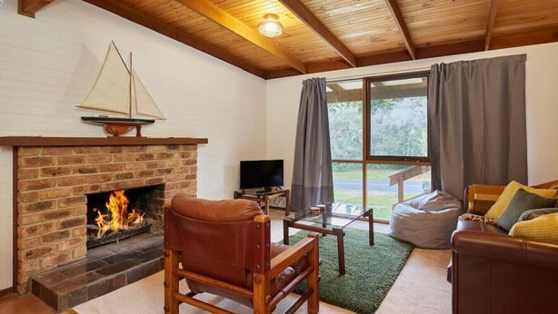 Ein gemütliches Wohnzimmer mit Kamin aus Ziegelsteinen, einem Ledersessel, einem Glastisch und einer Couch mit Kissen.