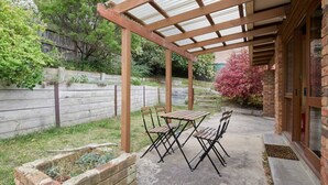 Eine überdachte Terrasse mit Tisch und Stühlen, einem Ziegelpflanzgefäß und einem Holzzaun im Hintergrund.
