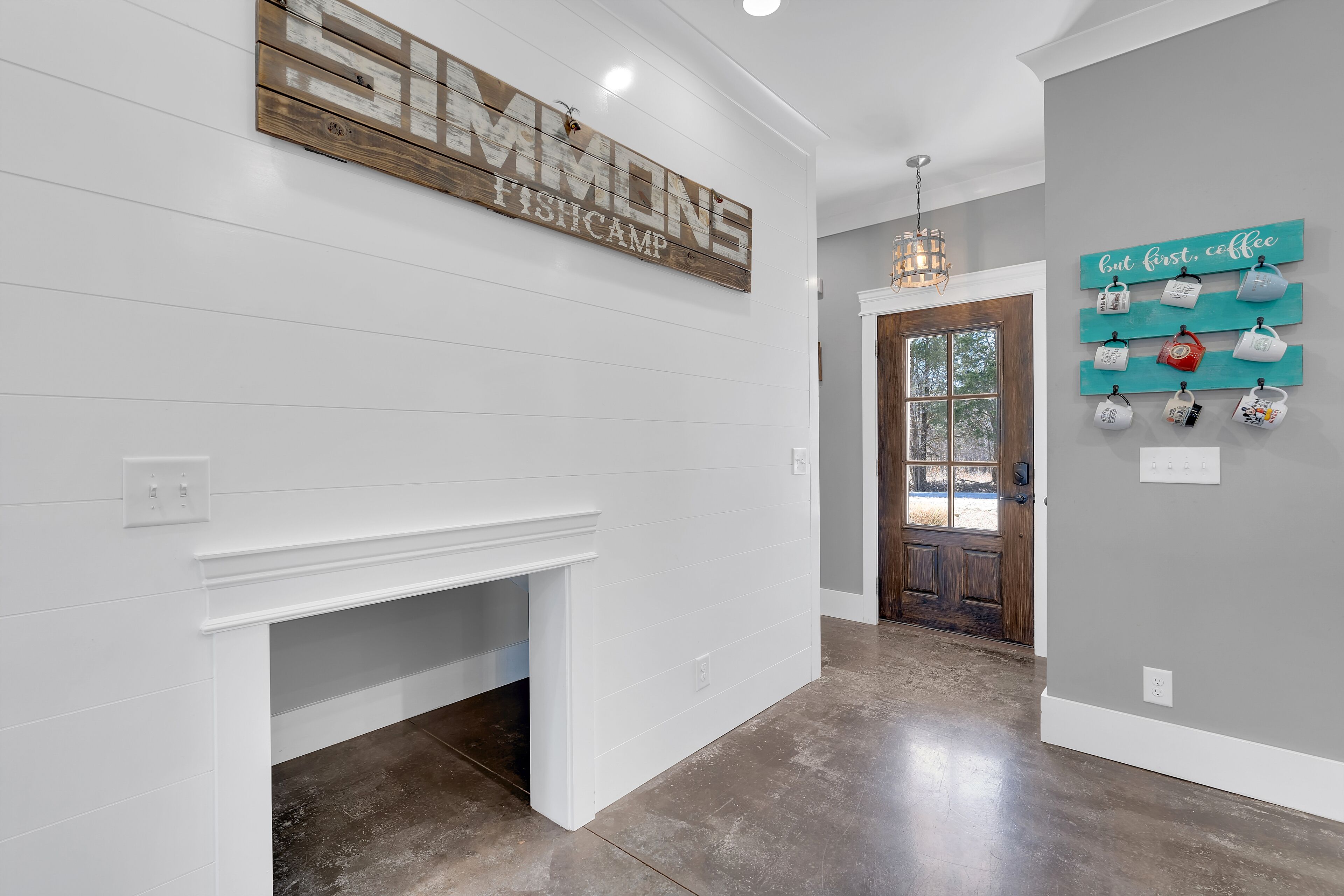 Un couloir avec un mur blanc, une enseigne en bois au-dessus d’une cheminée, et un mur turquoise orné de tasses.