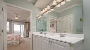 Une salle de bain avec un grand miroir, deux lavabos et un ventilateur de plafond.