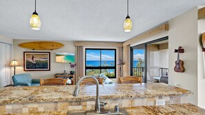 A spacious kitchen with a large island, granite countertops, and a view of the ocean. - MRR Presents Kaanapali Ali'i 282 -  Remodeled 8th Floor Corner 2BR w/ Partial Ocean AND Mountain Views! (Lahaina)