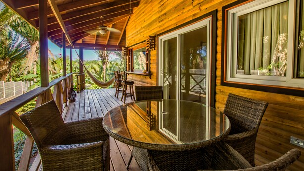 Une terrasse en bois avec une table en verre et des chaises en osier, donnant sur un jardin luxuriant.