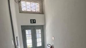 Un pasillo estrecho con una puerta doble, un extintor de incendios en la pared y un pequeño ventanal sobre la puerta.