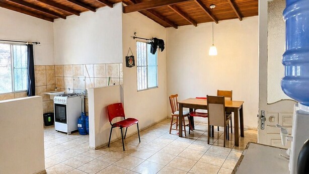 Una cocina con estufa a gas, un lavaplatos y un ventanal. Hay una zona de comedor con mesa y sillas.