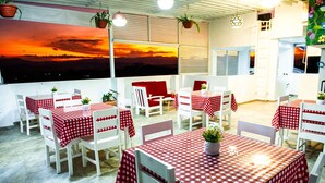 Un restaurante en la azotea con mesas y sillas a cuadros rojos y blancos, plantas en macetas y vistas al atardecer.