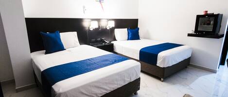 A hotel room with two beds, each with white bedding and blue accents, a black headboard, a small desk with a telephone, and a TV mounted on the wall.