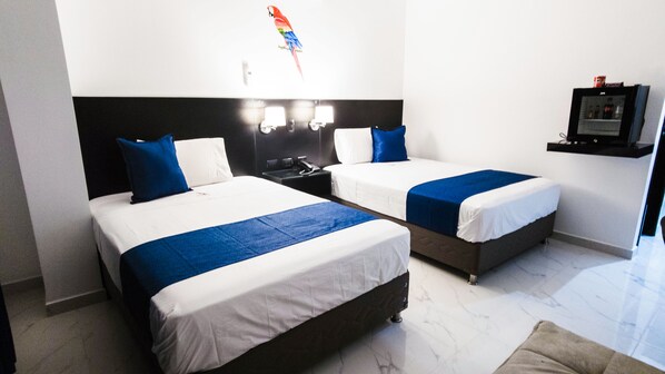 A hotel room with two beds, each with white bedding and blue accents, a black headboard, a small desk with a telephone, and a TV mounted on the wall. - Hotel Papagayo Boutique (Morales)