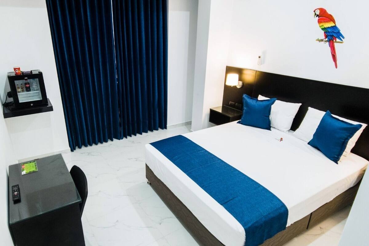 A hotel room with a bed, a desk, a chair, a TV, and a window with curtains.