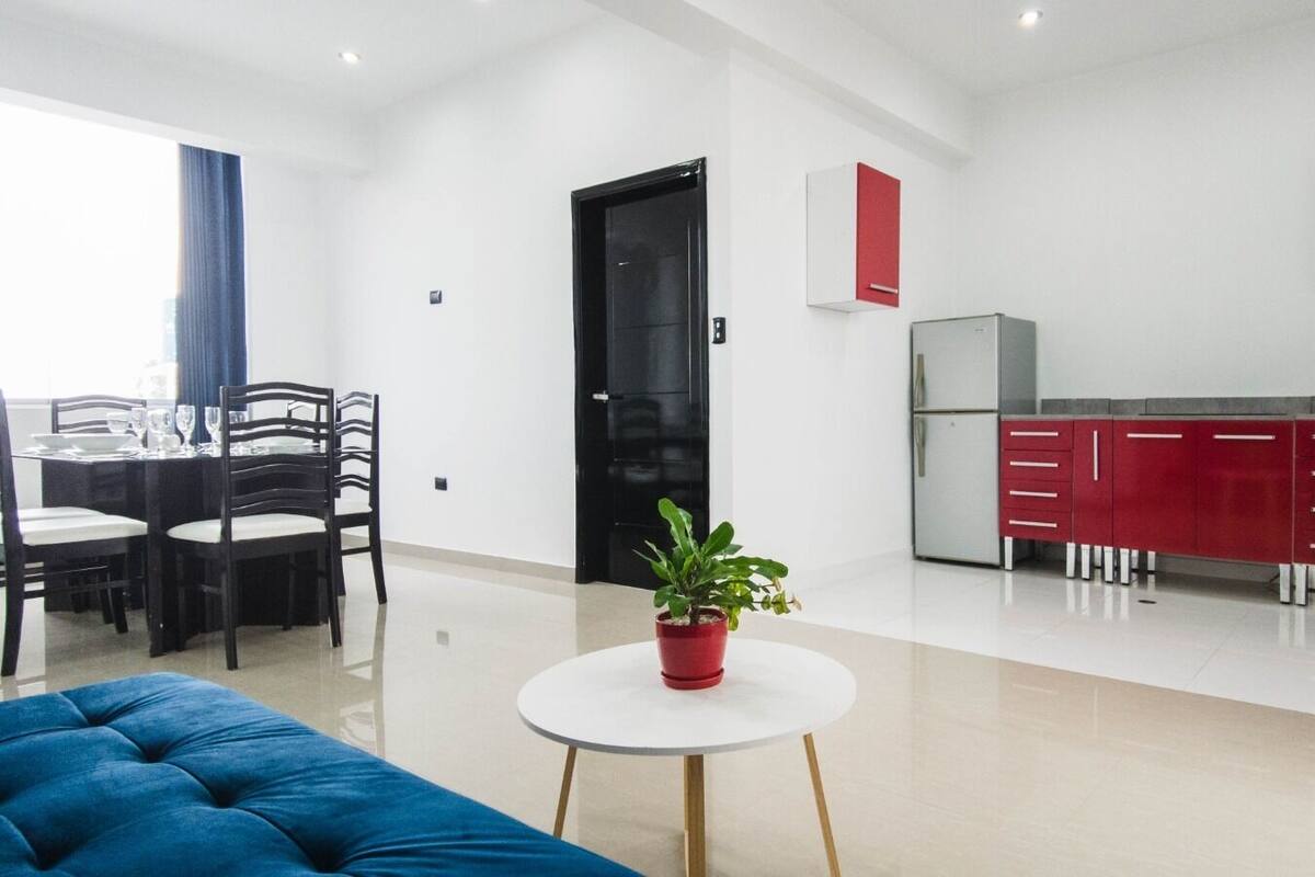 A modern apartment with a dining area, kitchen, and a blue sofa.