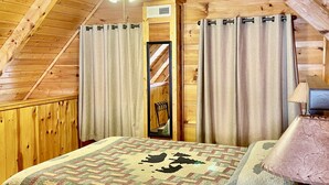 Ein gemütliches Schlafzimmer im Dachgeschoss mit Holzbalkendecke, einem Bett mit Bärenmotiv-Quilt, einem Deckenventilator und einem kleinen Tisch mit Lampe.