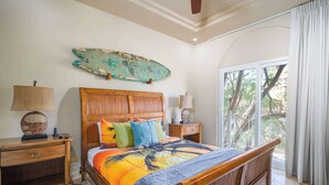 A bedroom with a wooden bed, a nightstand, a lamp, and a large window with a view of trees. - Matapalo 201 | Steps from Tamarindo Beach (Tamarindo)
