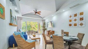 A spacious living area with wicker furniture, a dining table, and a ceiling fan. - Matapalo 201 | Steps from Tamarindo Beach (Tamarindo)