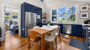 A modern kitchen with a dining area, stainless steel appliances, and large windows.