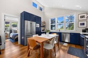 A modern kitchen with a dining area, stainless steel appliances, and large windows.