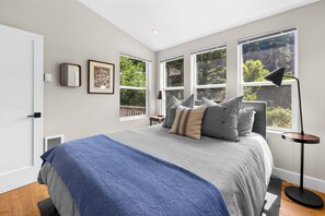 A bedroom with a bed, large windows, a bedside table, and a lamp.