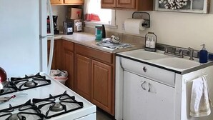 A kitchen with wooden cabinets, a white refrigerator, a stove, a sink, and a window with a cotton wreath decoration. - Cheyenne Cottage- Pet Friendly home, near Northwest College! (Powell)