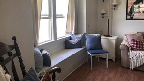 A cozy room with a built-in bench by a window, a white chair, a small table, and a couch with a throw blanket. - Cheyenne Cottage- Pet Friendly home, near Northwest College! (Powell)