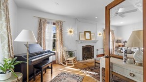 Een woonkamer met een piano, een open haard, een schommelstoel en een eethoek met een tafel en stoelen.