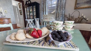 Een eettafel met een glazen blad, versierd met een bloemenonderzetter, een bord aardbeien, een kom braambessen en een stapel borden.