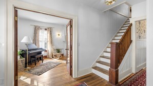 Een ruime woonkamer met een piano, een schommelstoel en een trap met houten leuningen.
