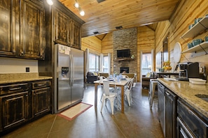 Une cuisine moderne avec une cheminée en pierre, des armoires en bois et un coin repas avec des chaises blanches.