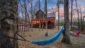 A rustic cabin with a wooden deck and a hammock.