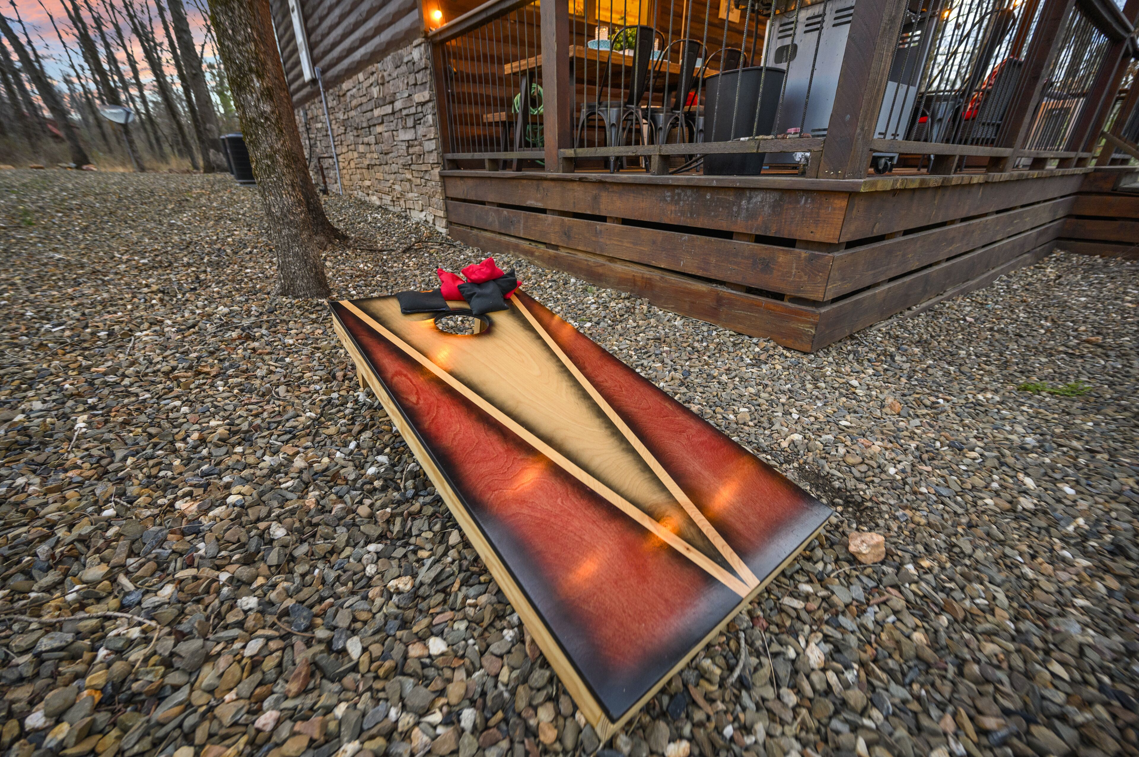 Un tobogán de madera con diseño rojo y negro, sobre una superficie de grava cerca de un edificio de fachada de piedra y una terraza de madera.