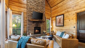 Un intérieur de chalet chaleureux avec une cheminée en pierre, des canapés en cuir et un téléviseur fixé au mur.