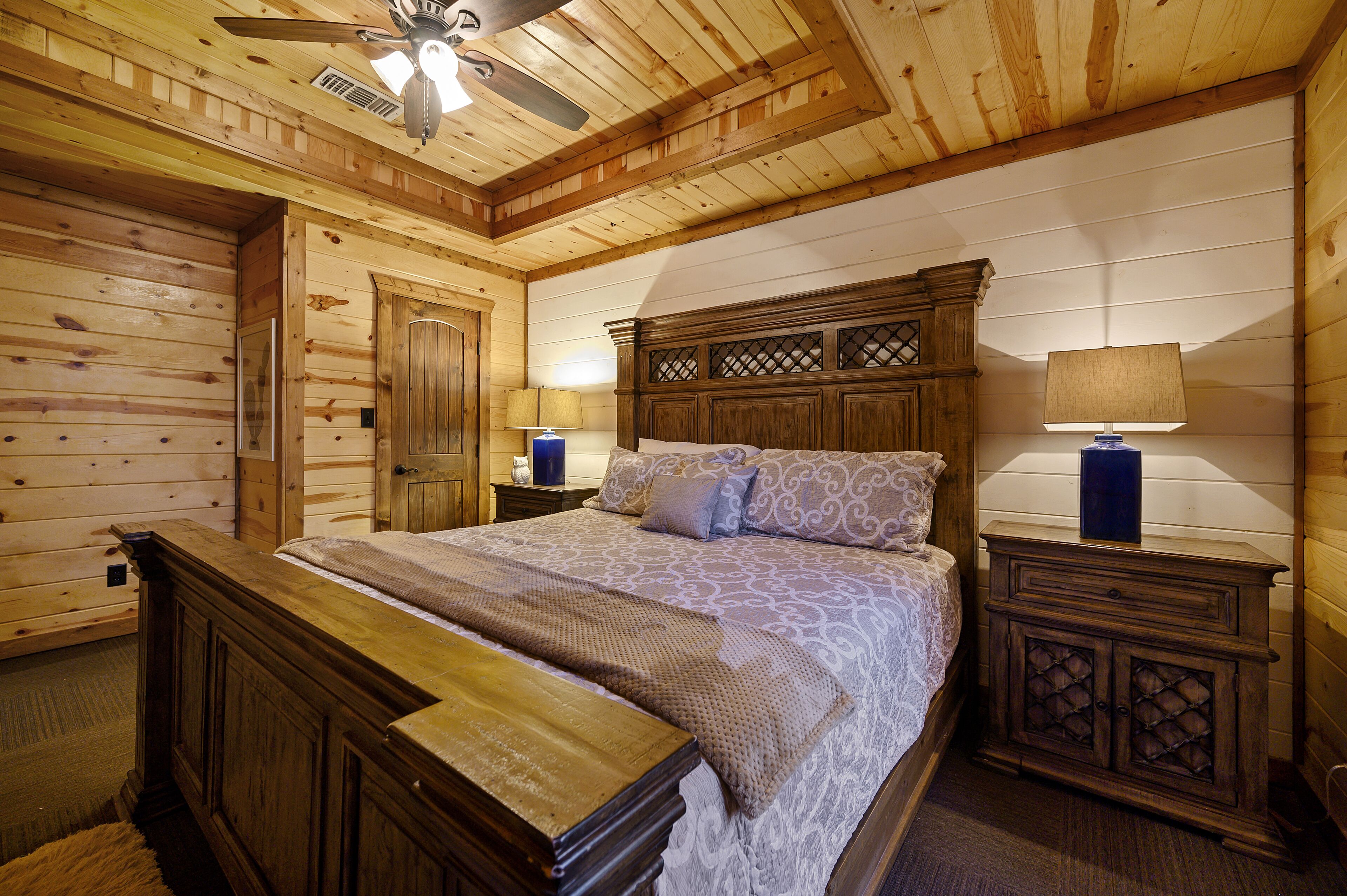 A wooden cabin-style bedroom with a bed, nightstands, and a ceiling fan.