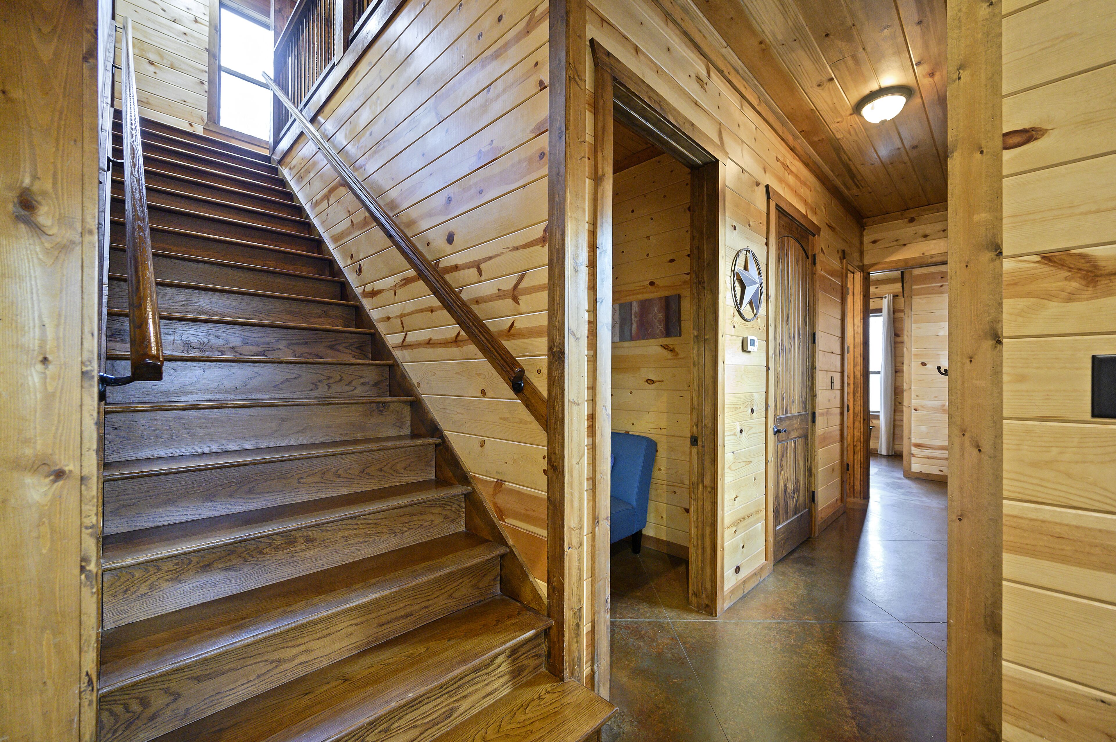 Una escalera de madera conduce a una habitación con una silla azul y un reloj en la pared.