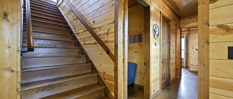 Una escalera de madera conduce a una habitación con una silla azul y un reloj en la pared.