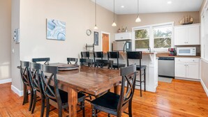 Un coin repas avec une table et des chaises en bois, une cuisine avec des meubles blancs et une fenêtre équipée de stores.