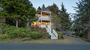 Une maison en bois à deux étages, dotée d’un balcon et entourée d’une forêt dense.