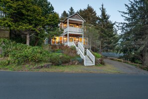 Une maison en bois à deux étages, dotée d’un balcon et entourée d’une forêt dense.