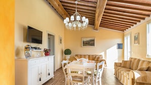 A dining area with a white table, chairs, a chandelier, a television, and a sofa.